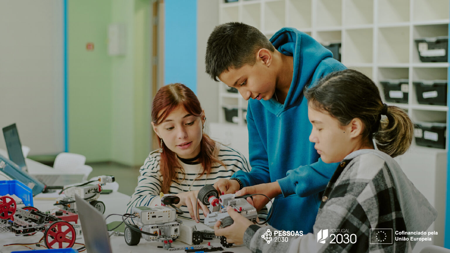 Três jovens a montar kits de robótica e eletrónica numa sala de aula